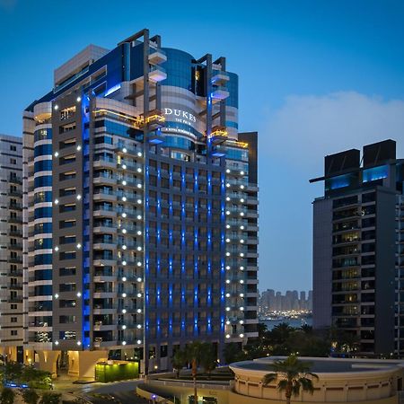 Dukes The Palm, A Royal Hideaway Hotel Dubai Esterno foto The photo shows a modern high-rise building, which appears to be a hotel or residential complex. The design features sleek lines and a glass façade, illuminated with blue lighting that enhances its contemporary look. Surrounding the main building are