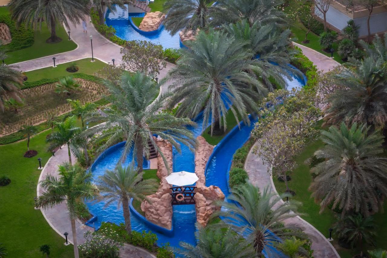 Dukes The Palm, A Royal Hideaway Hotel Dubai Esterno foto The photo shows a beautifully landscaped outdoor area featuring a winding water channel with vibrant blue water. Flanking the waterway are lush green palm trees and other vegetation, creating a tropical ambiance. There are also stone features along t
