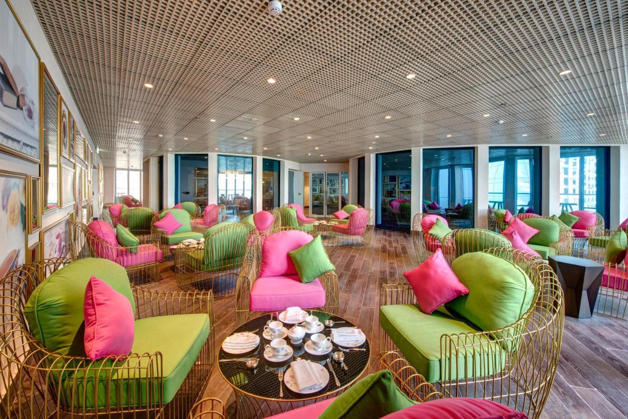 Dukes The Palm, A Royal Hideaway Hotel Dubai Esterno foto The photo shows a stylish and modern lounge area. The seating consists of unique chairs and sofas that combine bright green and pink colors, adorned with matching cushions. The space has a contemporary design, featuring a wooden floor and large windo