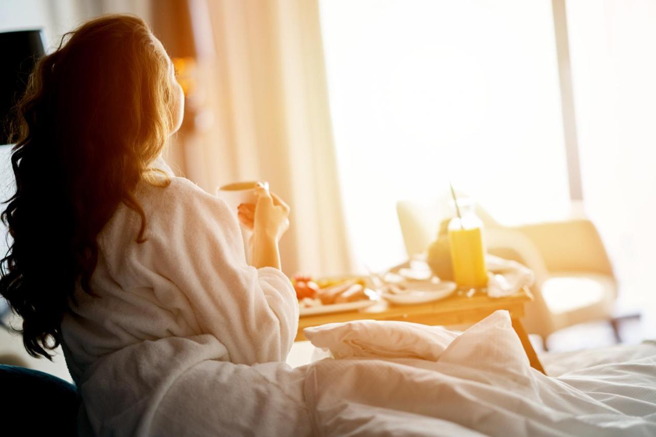 Dukes The Palm, A Royal Hideaway Hotel Dubai Esterno foto The image shows a person sitting on a bed, wearing a cozy bathrobe. They appear to be enjoying a moment of relaxation, possibly sipping a drink from a cup. In front of them, there is a tray with food and a drink, suggesting a breakfast or brunch setu