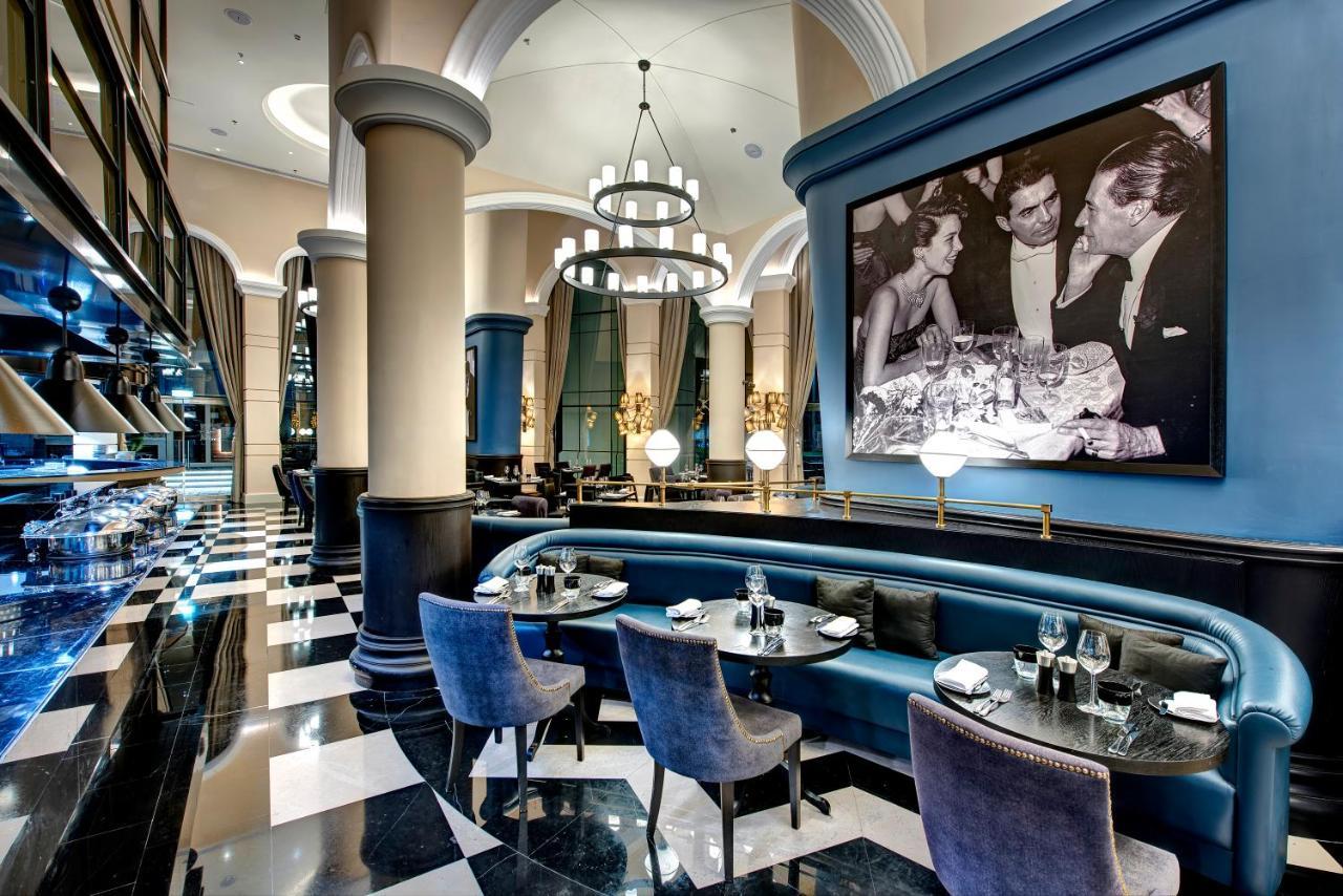 Dukes The Palm, A Royal Hideaway Hotel Dubai Esterno foto The image shows an elegant restaurant interior with a sophisticated design. The space features high ceilings, large columns, and a combination of blue and black color schemes. There is a stylish seating area with upholstered chairs and tables set for