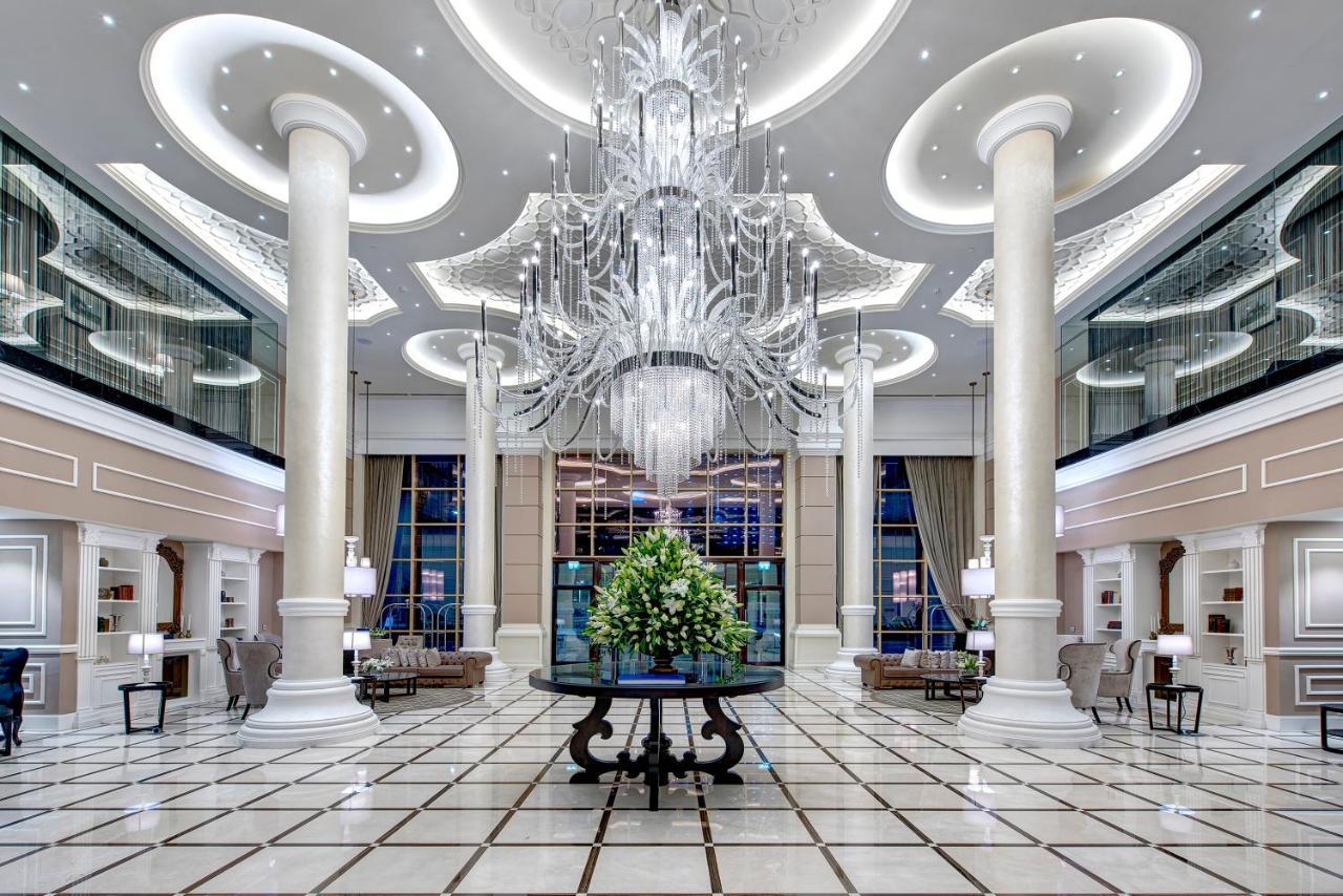 Dukes The Palm, A Royal Hideaway Hotel Dubai Esterno foto The photo depicts the interior of a luxurious lobby or hotel entrance. It features tall, elegant columns and a grand chandelier hanging from the ceiling, illuminating the space with soft light. The floor is tiled with a geometric pattern, enhancing t