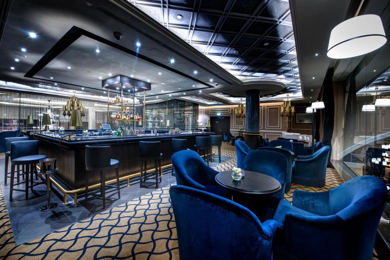 Dukes The Palm, A Royal Hideaway Hotel Dubai Esterno foto The photo shows an upscale bar or lounge area. The interior features modern design elements with elegant lighting. There is a stylish bar counter with a variety of drinks, and seating consists of plush blue armchairs arranged around small tables. The