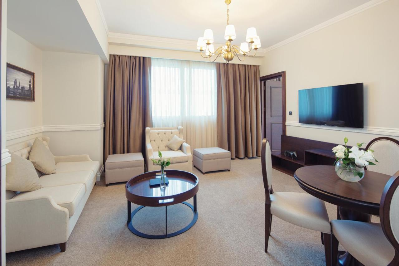 Dukes The Palm, A Royal Hideaway Hotel Dubai Esterno foto The photo shows a well-furnished living space. There is a light-colored sofa, a comfortable armchair, and an ottoman, arranged around a round wooden coffee table. A dining table with chairs is also present. The room features a large window draped wit