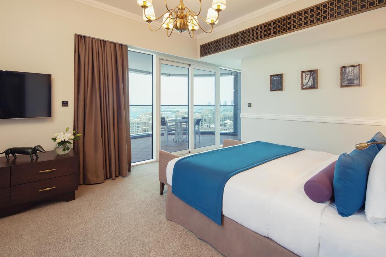 Dukes The Palm, A Royal Hideaway Hotel Dubai Esterno foto The photo shows a stylish and modern bedroom. It features a large bed with a blue and purple throw blanket, complemented by decorative pillows. Next to the bed, there is a dark wooden nightstand. A flat-screen TV is mounted on the wall opposite the b