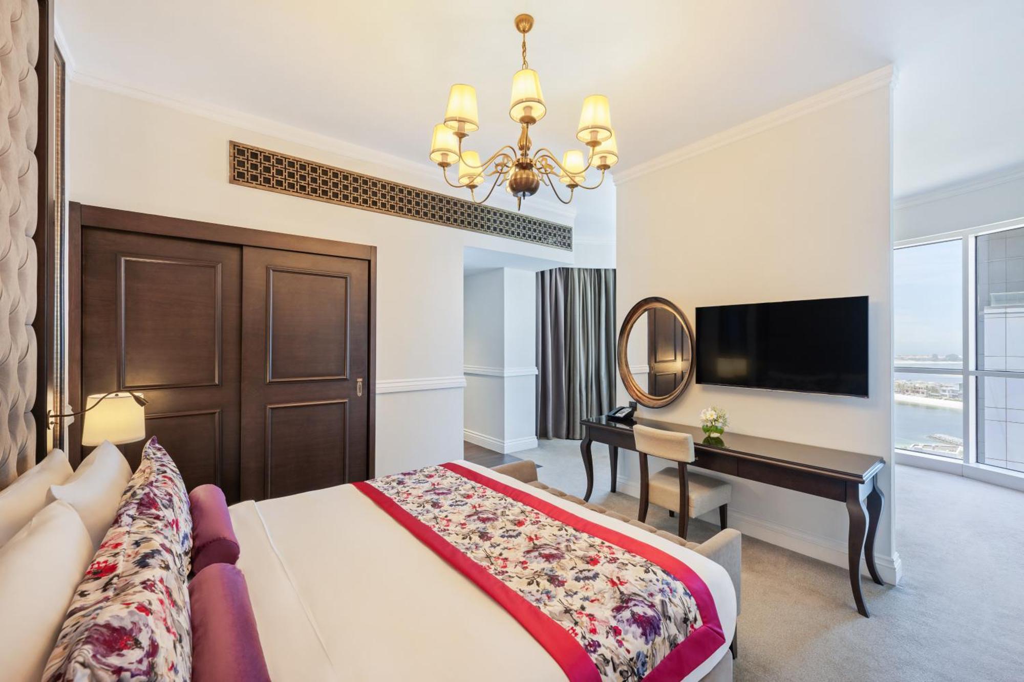 Dukes The Palm, A Royal Hideaway Hotel Dubai Esterno foto The photo shows an elegantly furnished bedroom. The room features a large bed with decorative pillows and a vibrant bedspread. There's a stylish chandelier hanging from the ceiling, adding a touch of sophistication. To one side, there are double door