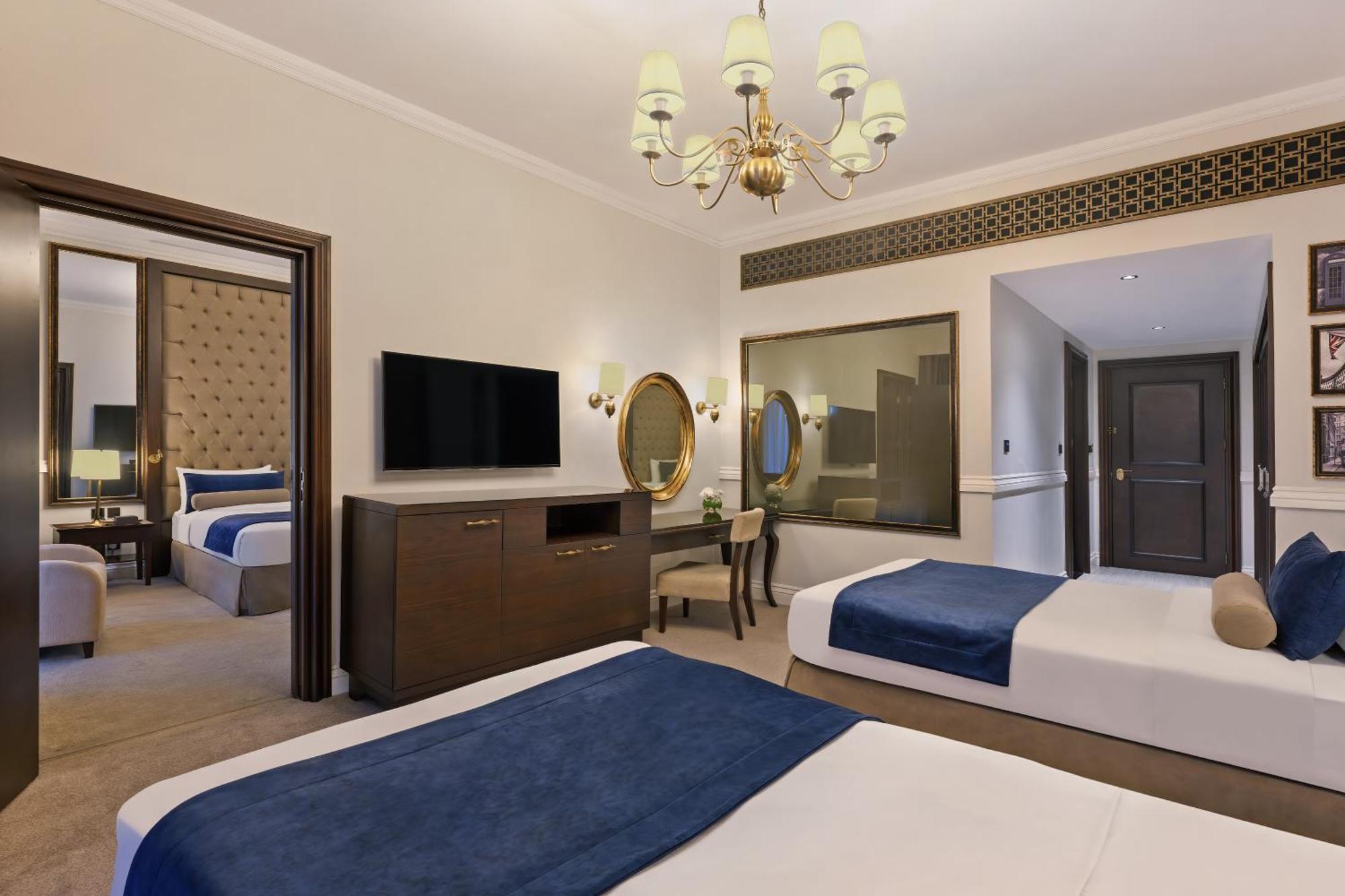 Dukes The Palm, A Royal Hideaway Hotel Dubai Esterno foto The photo shows a hotel room featuring two beds with blue and white bedding. There’s a light-colored carpet on the floor. A chandelier hangs from the ceiling, providing illumination. A wooden dresser is positioned against one wall, with a flat-screen