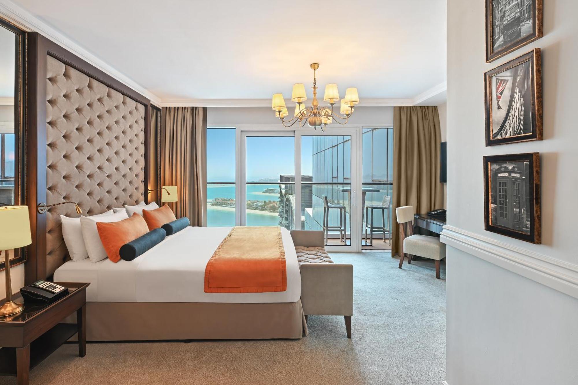 Dukes The Palm, A Royal Hideaway Hotel Dubai Esterno foto The photo shows a luxurious hotel room featuring modern decor. The room includes a large bed with a tufted headboard, adorned with orange and black accent pillows. There are large windows that offer a view of the outdoors, with sheer curtains and dar