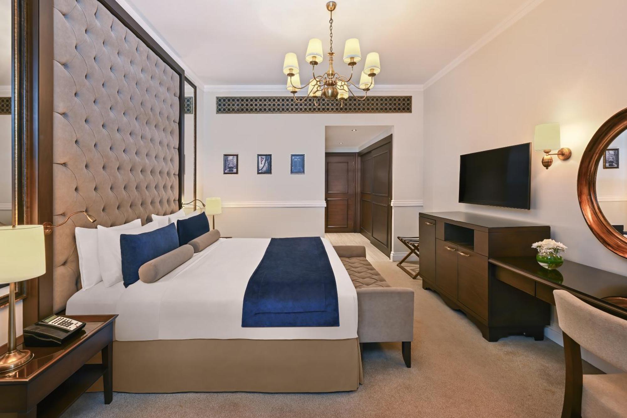 Dukes The Palm, A Royal Hideaway Hotel Dubai Esterno foto The image shows a hotel room featuring a large, neatly arranged bed with decorative pillows. The headboard is tufted and upholstered in a beige fabric. There is a small sofa or bench at the foot of the bed in a contrasting color. The room is well-lit