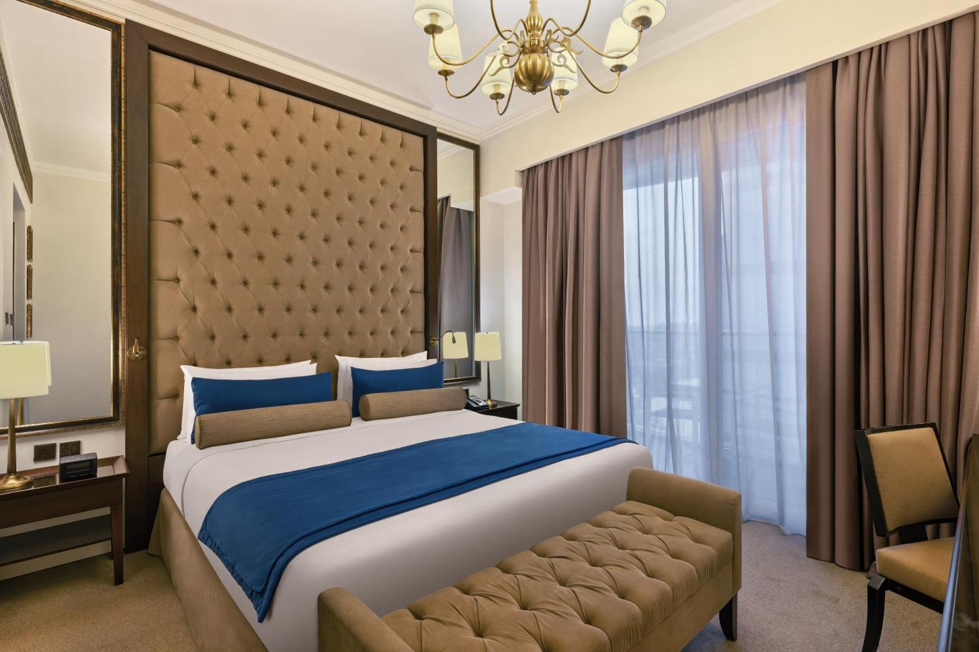 Dukes The Palm, A Royal Hideaway Hotel Dubai Esterno foto The photo depicts a stylish hotel room with a modern design. It features a large bed with a tufted headboard upholstered in a tan color. The bed is dressed with white sheets and dark blue and beige decorative pillows. On either side of the bed, there