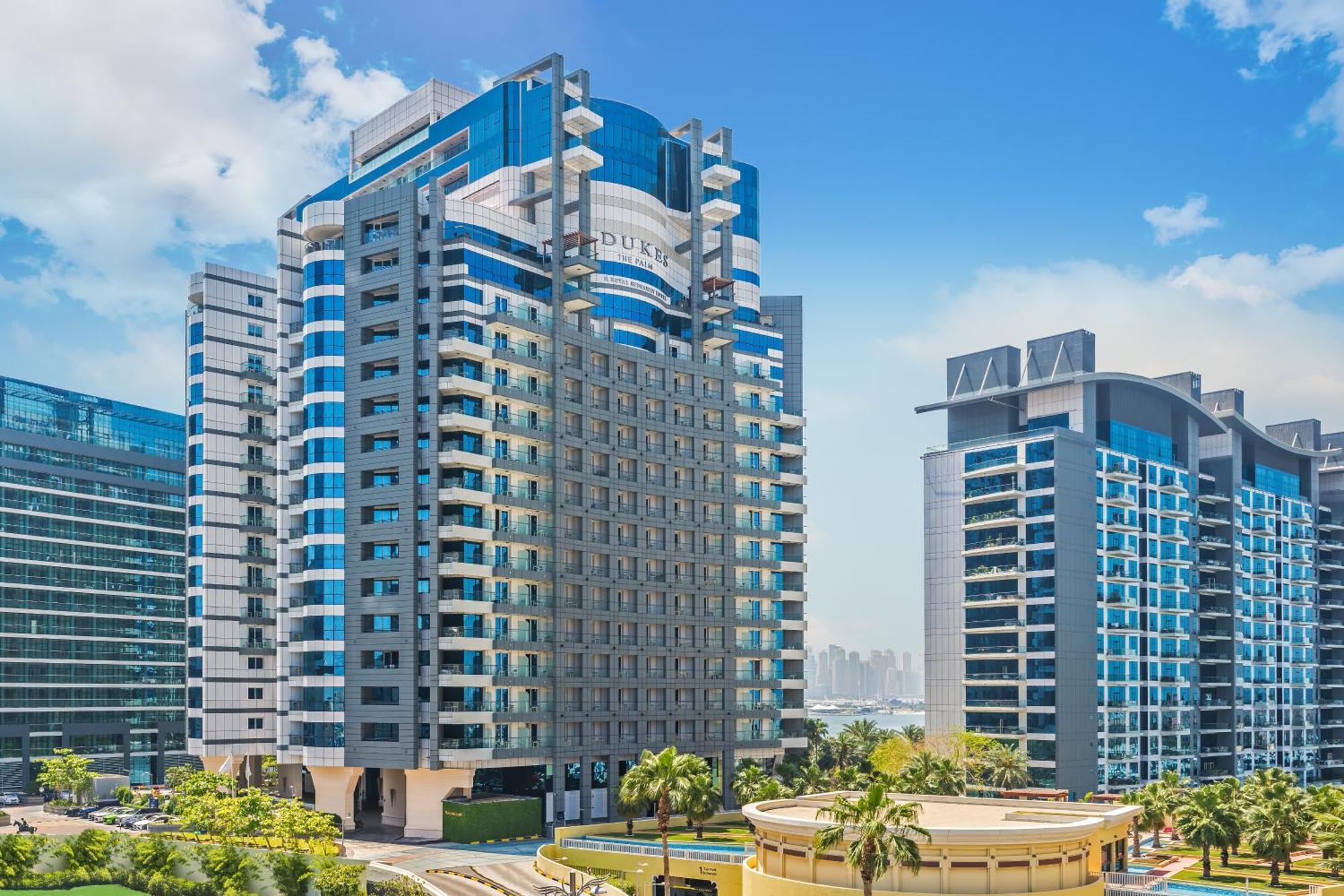 Dukes The Palm, A Royal Hideaway Hotel Dubai Esterno foto The photo depicts a modern urban skyline featuring several high-rise buildings. Prominent in the foreground is a sleek, multi-story structure with a combination of glass and concrete elements, showcasing a contemporary architectural style. The buildi