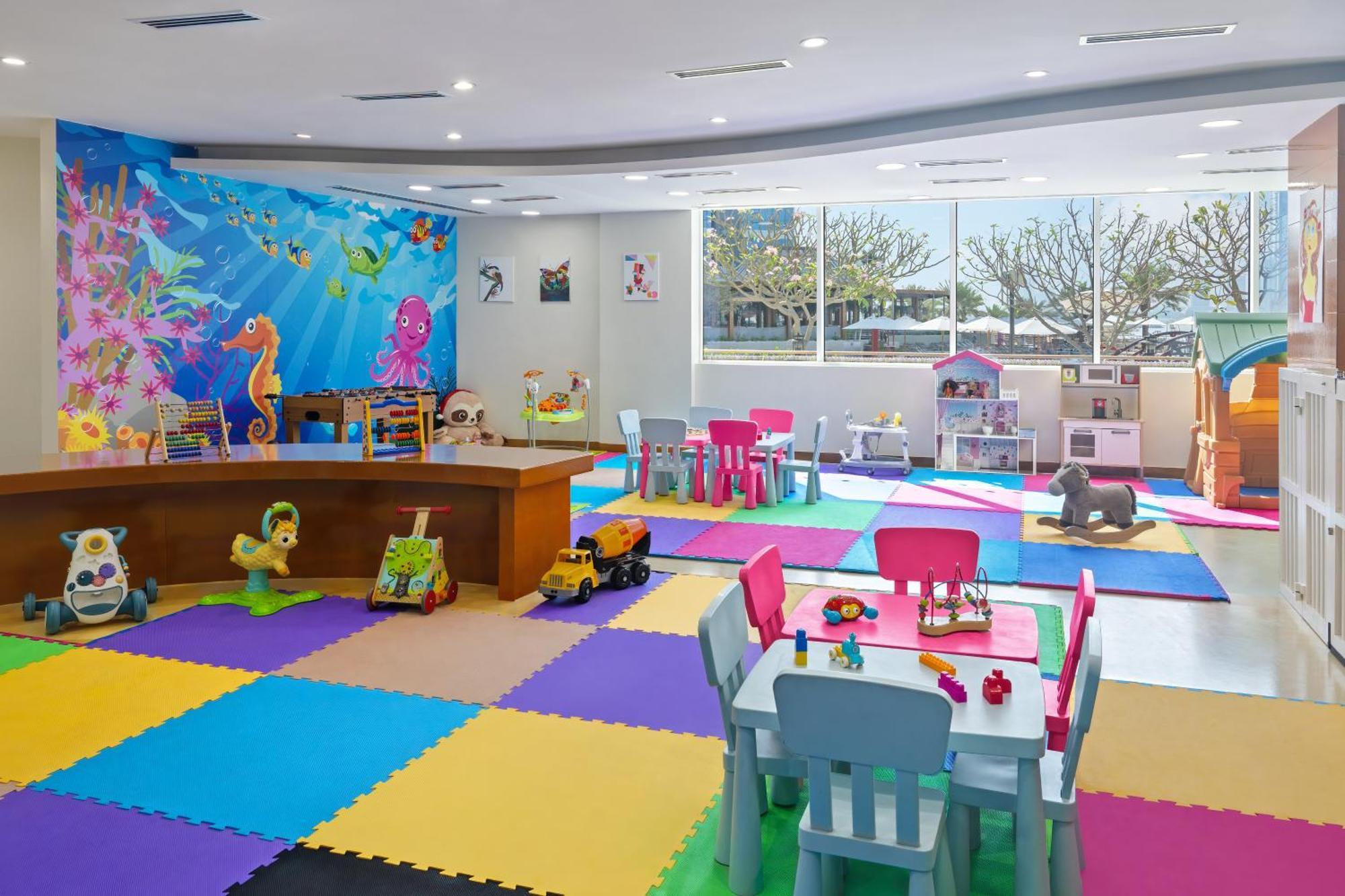 Dukes The Palm, A Royal Hideaway Hotel Dubai Esterno foto The photo shows a bright and colorful children's playroom. The floor is covered with interlocking foam mats in various colors, including blue, green, yellow, and purple. There is a large table made of wood at the center, surrounded by colorful chairs