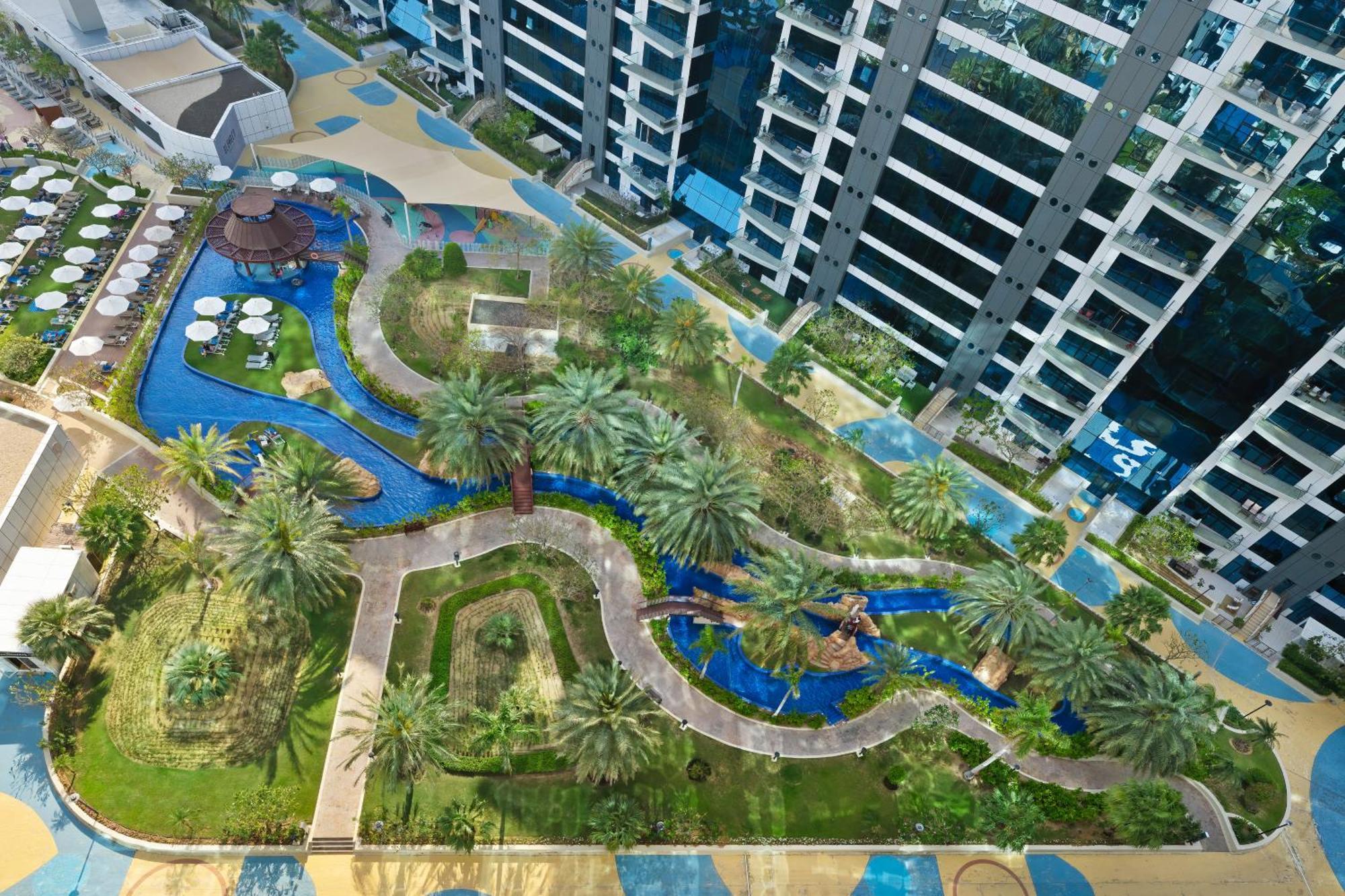 Dukes The Palm, A Royal Hideaway Hotel Dubai Esterno foto The photo showcases a landscaped area featuring a winding waterway that meanders through a garden-like setting. Surrounding the water are patches of greenery, including palm trees and various plants. There are pathways lined with tiles, and several c
