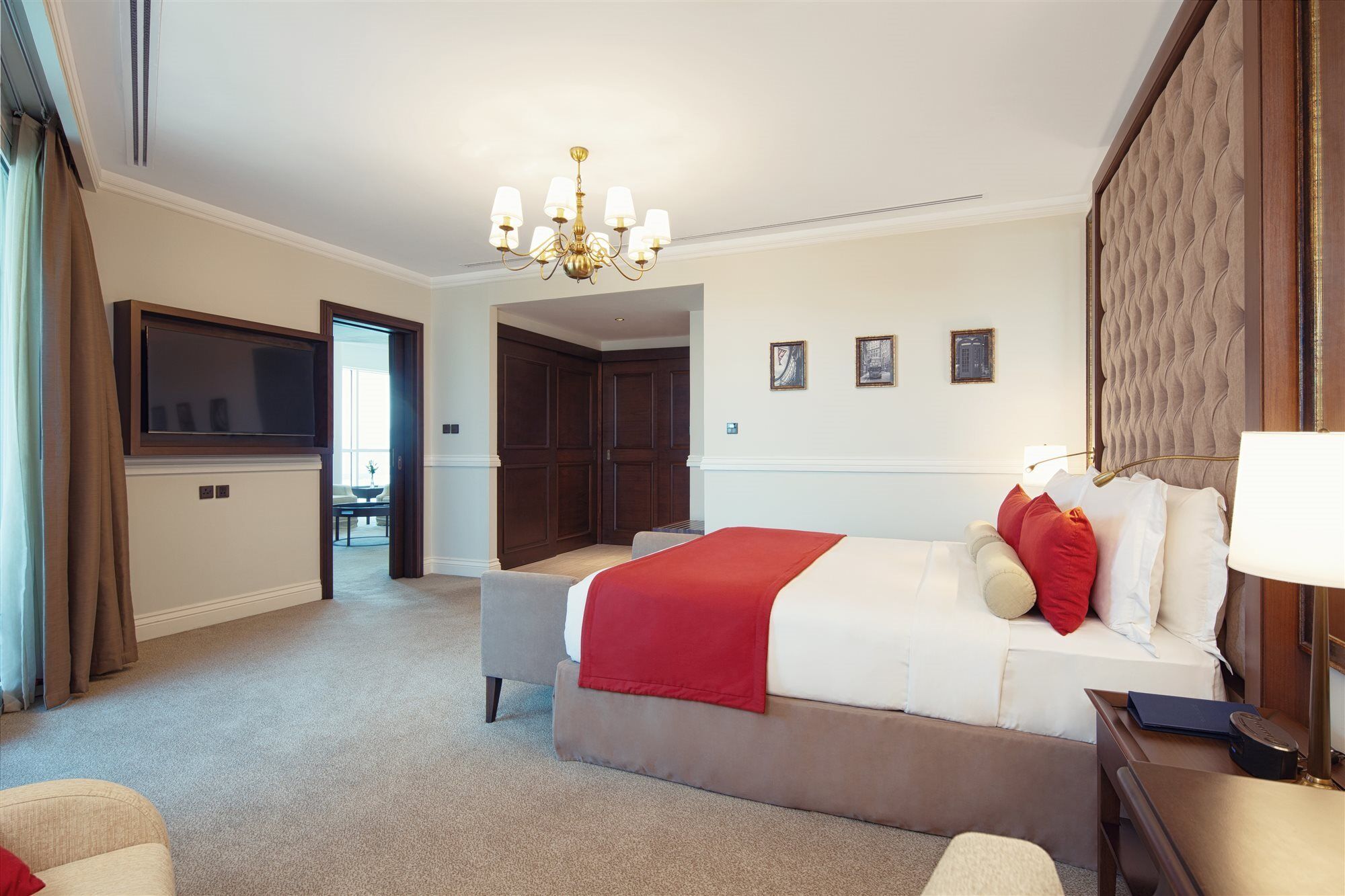 Dukes The Palm, A Royal Hideaway Hotel Dubai Esterno foto The photo shows a well-appointed hotel room. It features a large bed with white linens and red accent pillows. There is a comfortable seating area with a chair, and a side table. A chandelier hangs from the ceiling, providing lighting. On the wall be
