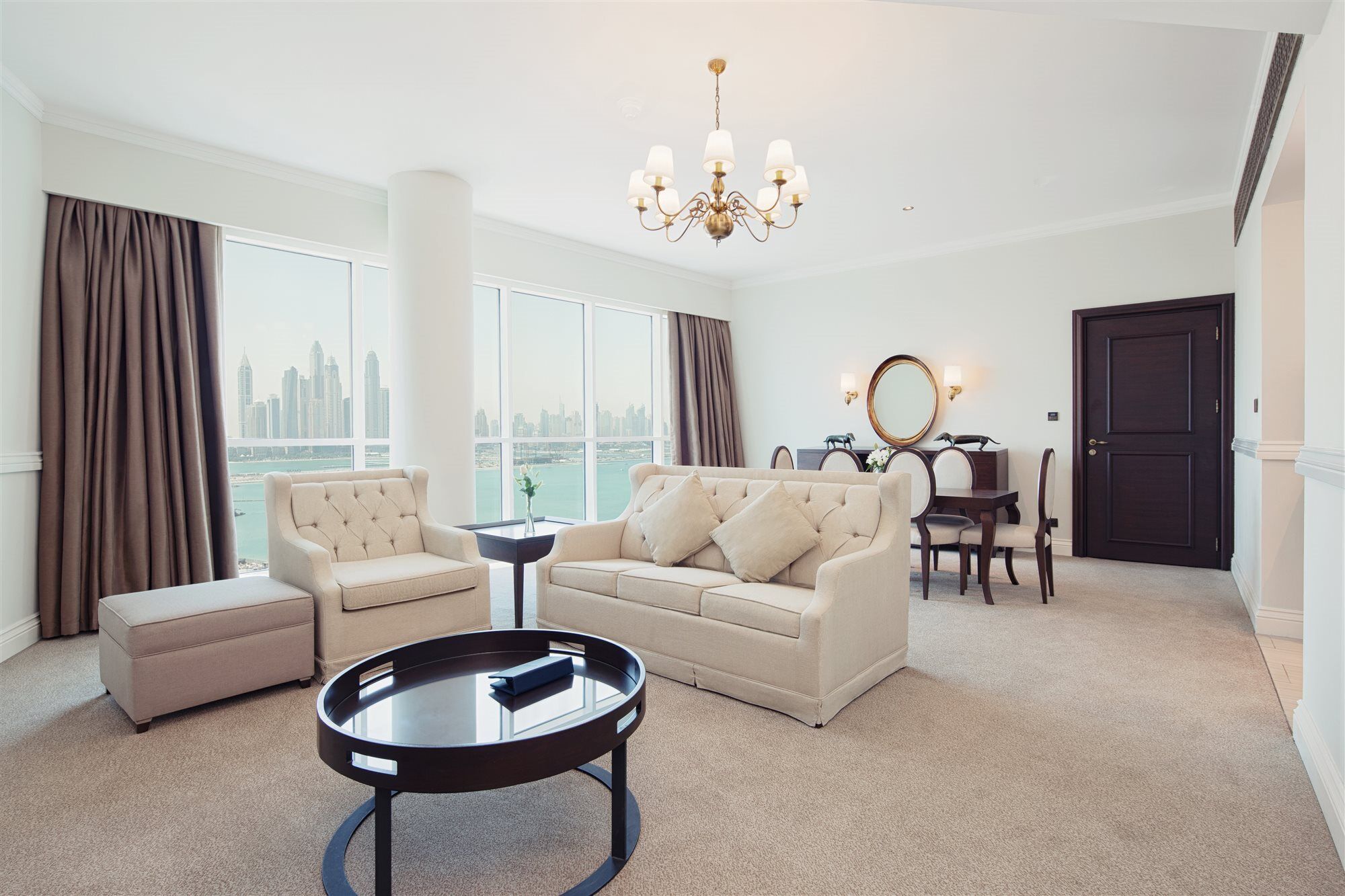 Dukes The Palm, A Royal Hideaway Hotel Dubai Esterno foto The photo shows a stylish and modern living room. It features a comfortable light-colored sofa with decorative cushions, a round black coffee table in the center, and a small matching stool nearby. There are large windows with views of a city skyline